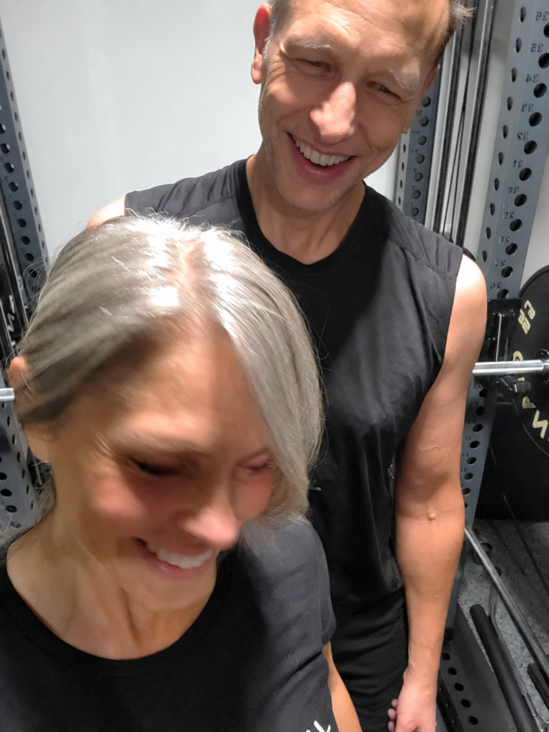 Erin and her husband laughing together in their home gym during a strength training session.